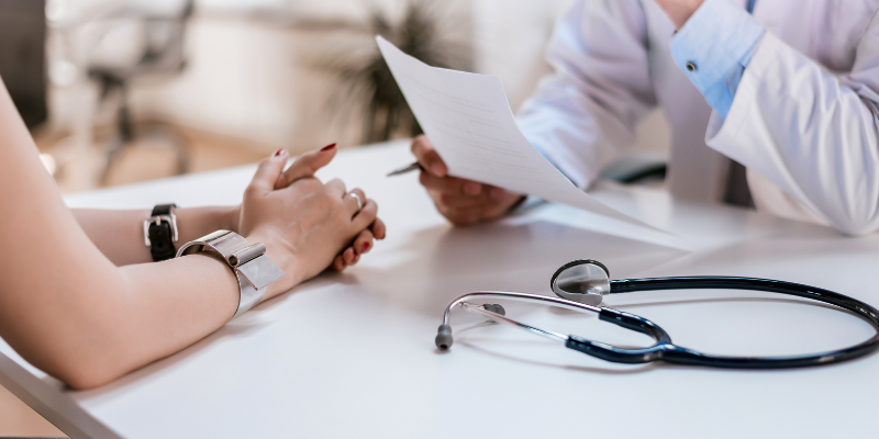 A doctor sitting at a table holding papers with a stethoscope on the table and folded hands of a pet parent over the table. Animal Emergency & Referral Center of Minnesota.