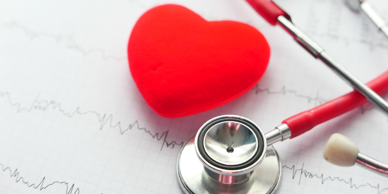 A toy heart with a stethoscope on top of a printed off ECG reading.