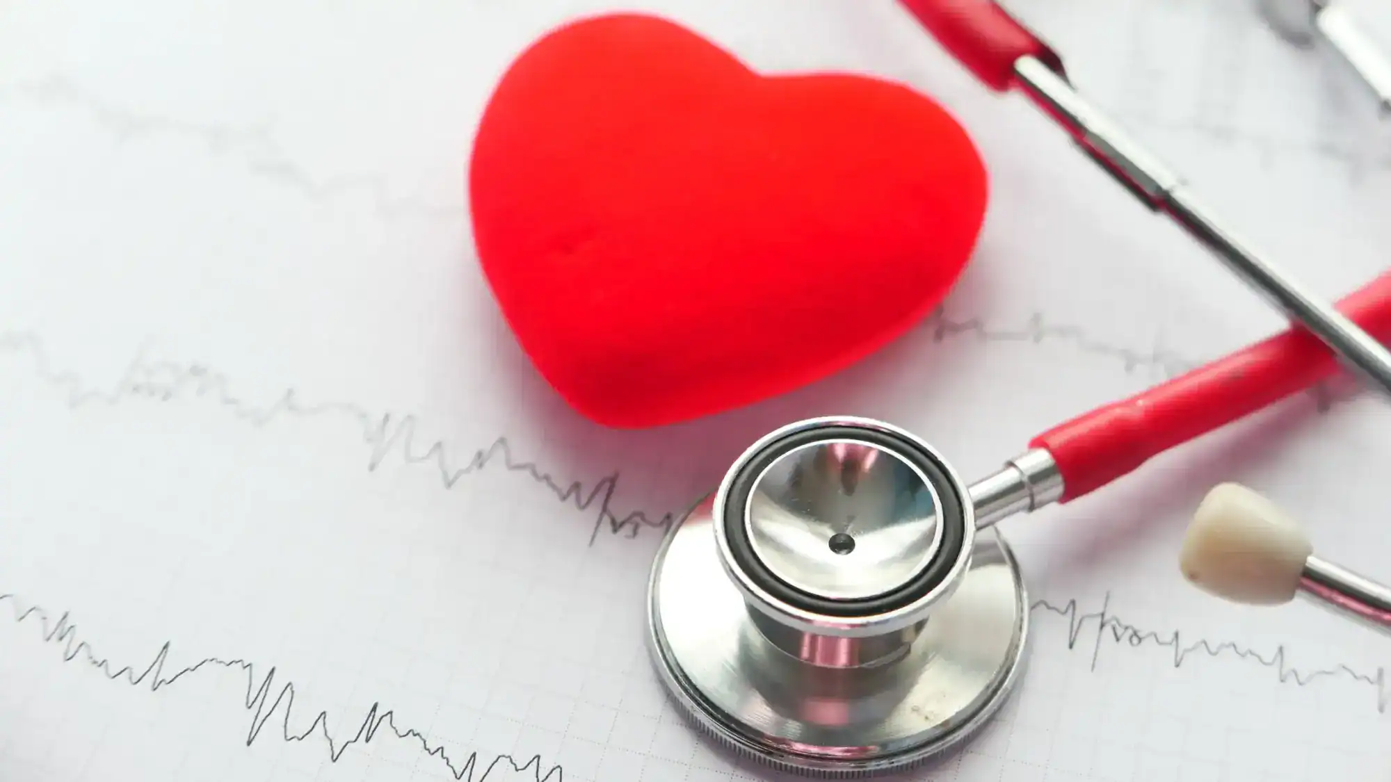 A toy heart with a stethoscope on top of a printed off ECG reading.