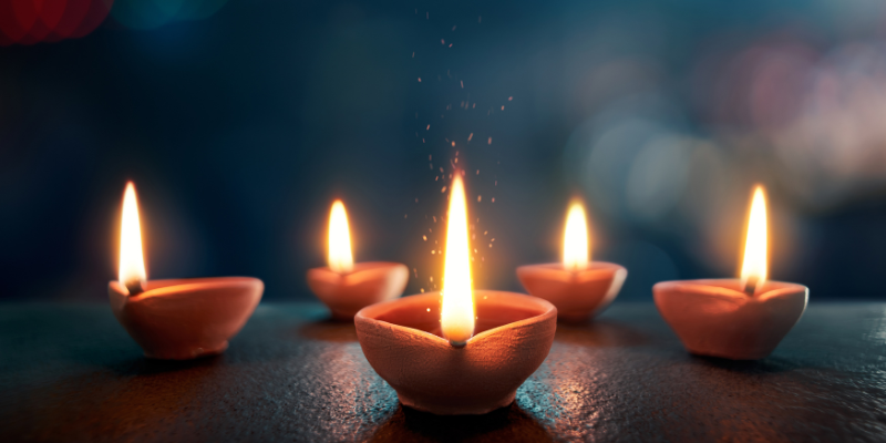 A line of lit diyas with a dark background.