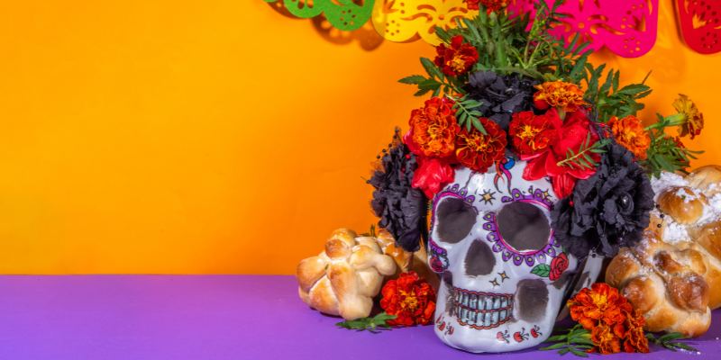 A decorated calavera with a floral bouquet against a vivid orange backdrop.