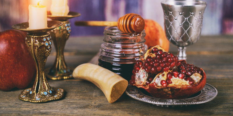 A table spread for Rosh Hashanah that includes a candle, honey, a shofar, and a pomegranate.