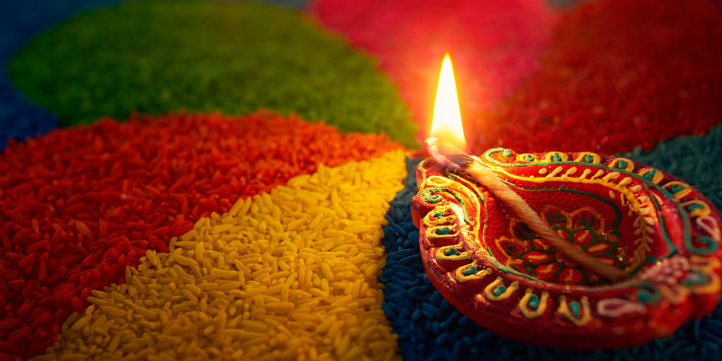 A close-up of a colorful rangoli with a lit diya.