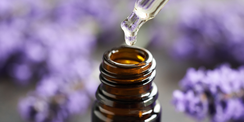 A bottle of essential oils in front of purple flowers.