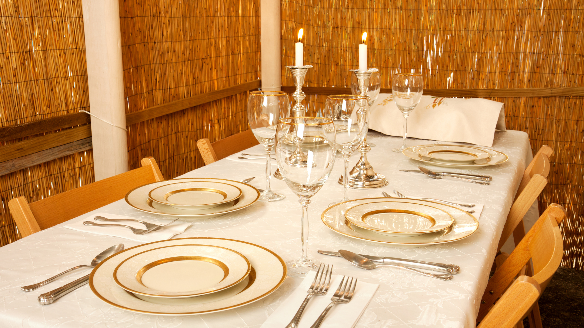 A set table with dinnerware, flatware, and candles inside a large sukkah. 