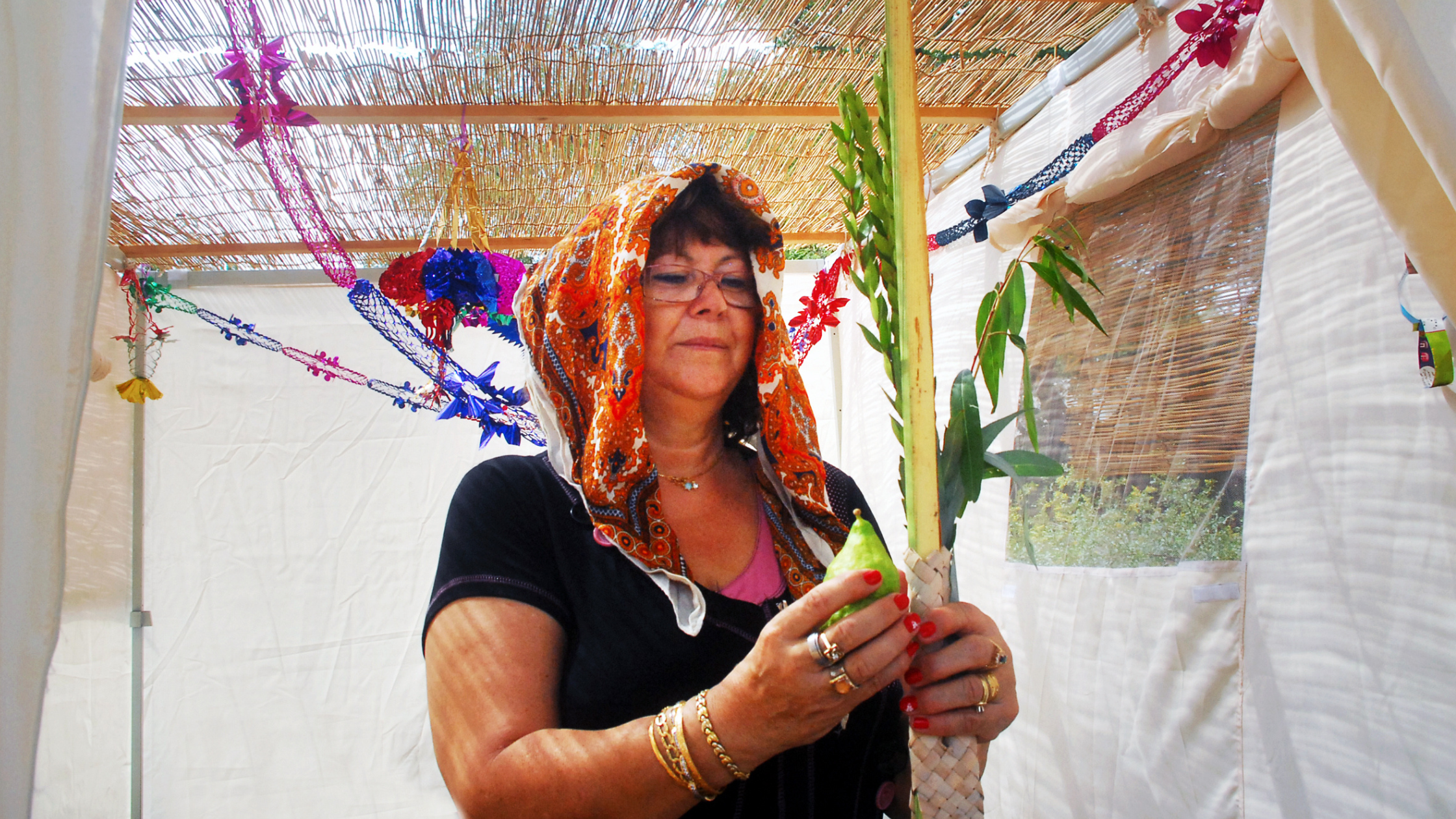 A woman inside a decorated sukkah holding citron.