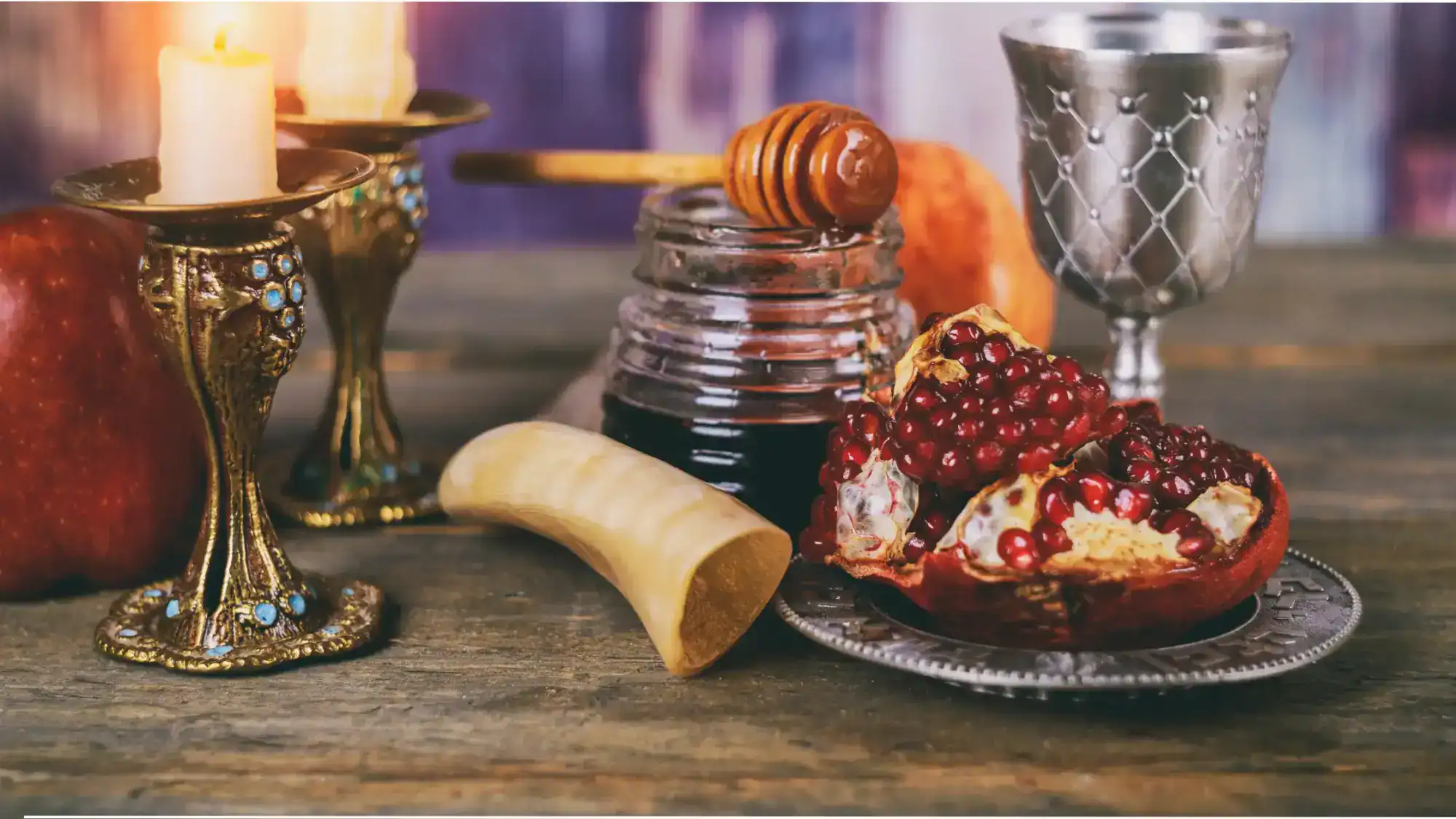 A table spread for Rosh Hashanah that includes a candle, honey, a shofar, and a pomegranate.