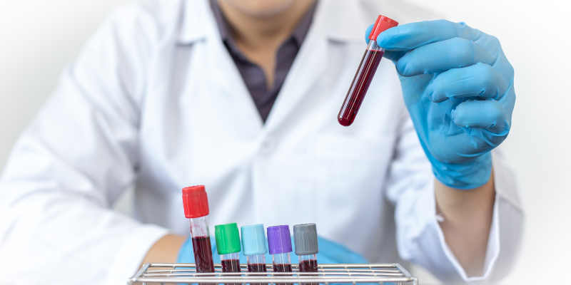 A lab tech with gloved hands holding up a sample tube with blood.