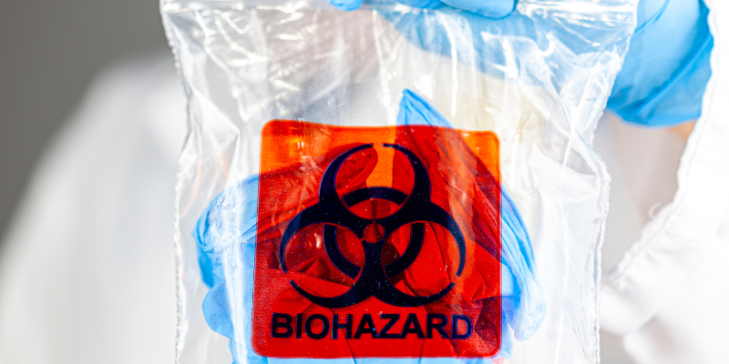 Gloved hands holding up a plastic bag with a biohazard label.