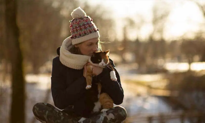 Woman holding and kissing her cat outside